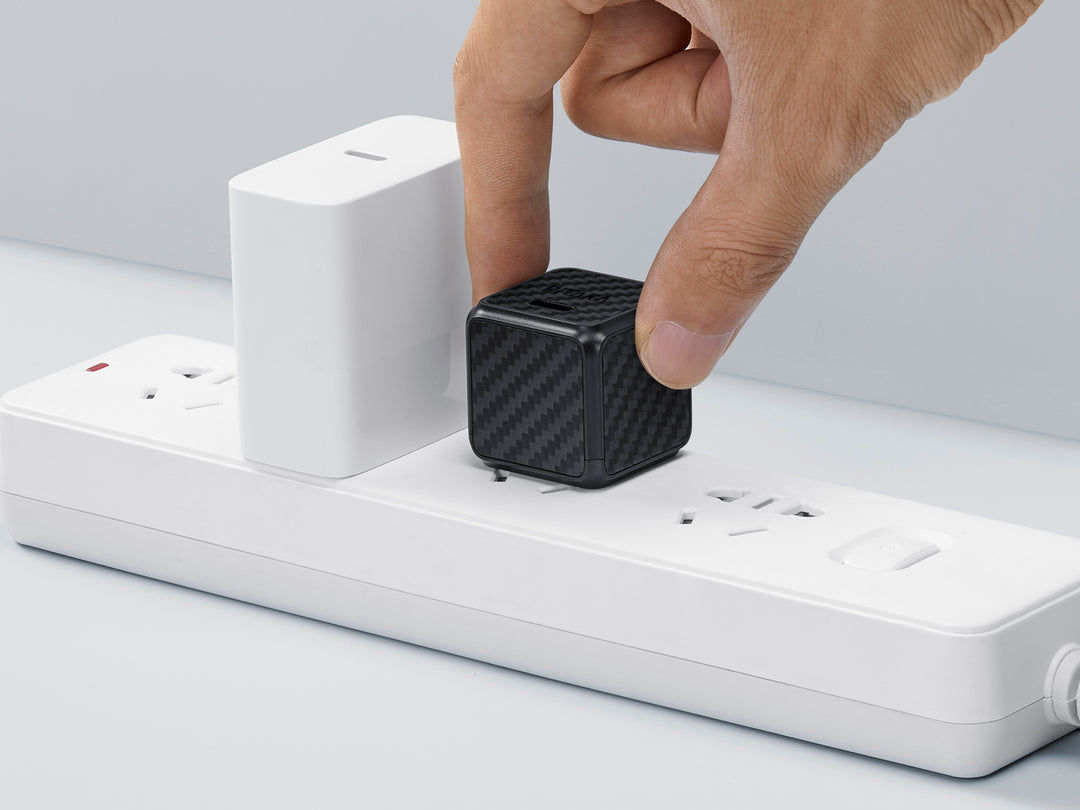 Hand unplugging a stylish carbon fiber patterned GaN charger from a white power strip.