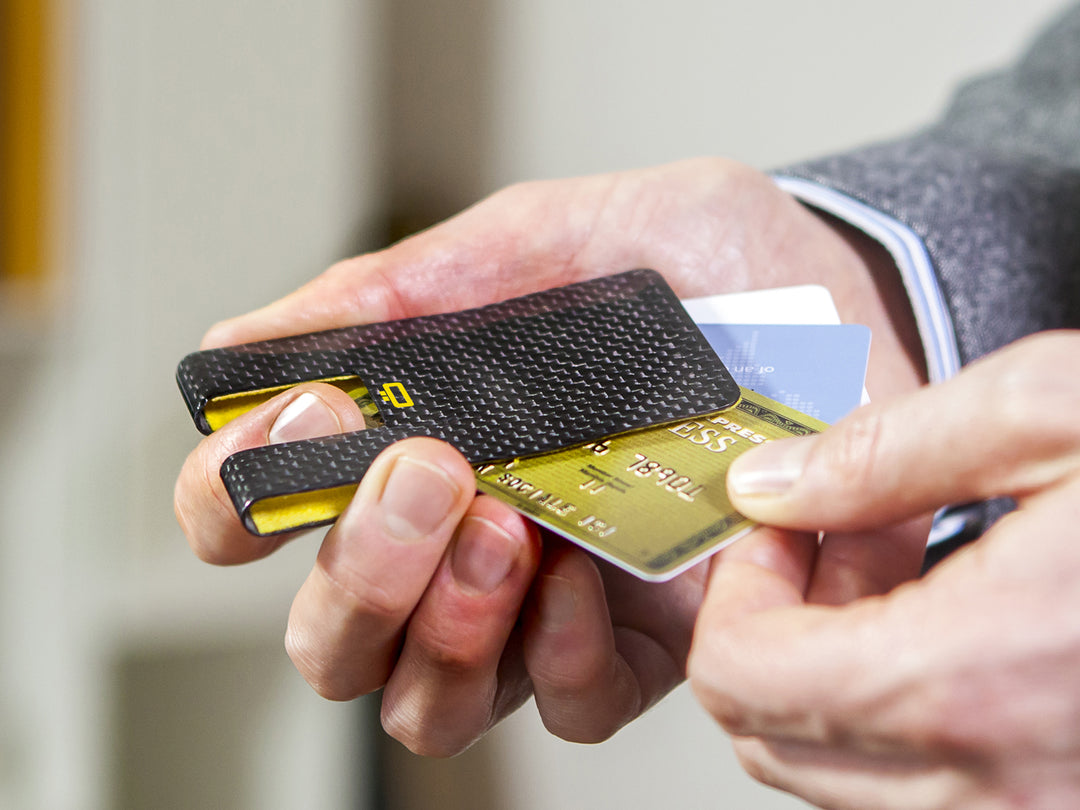 Person holding a carbon fiber card clip with multiple cards partially inserted, demonstrating its use.