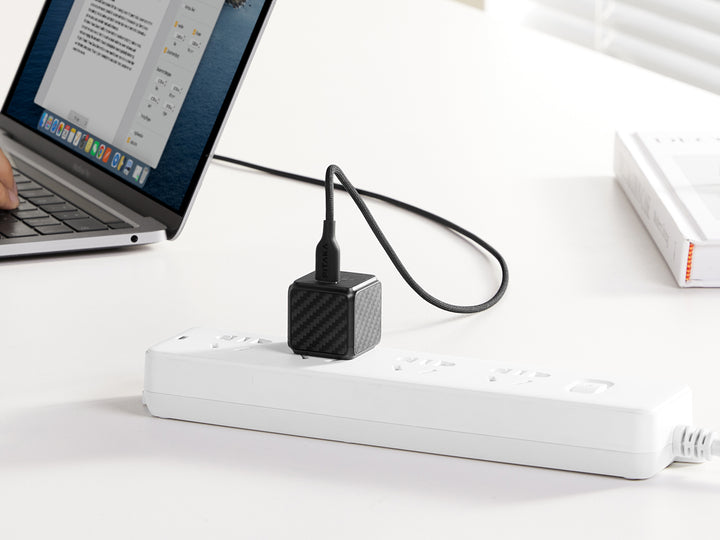 Carbon fiber patterned GaN charger connected to a laptop, offering a modern charging solution.