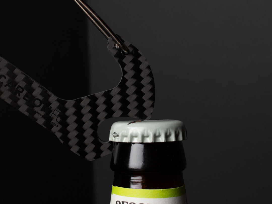 The CarbonFG Carabiner Bottle Opener in use, demonstrating its functionality and sleek design as it opens a bottle cap.