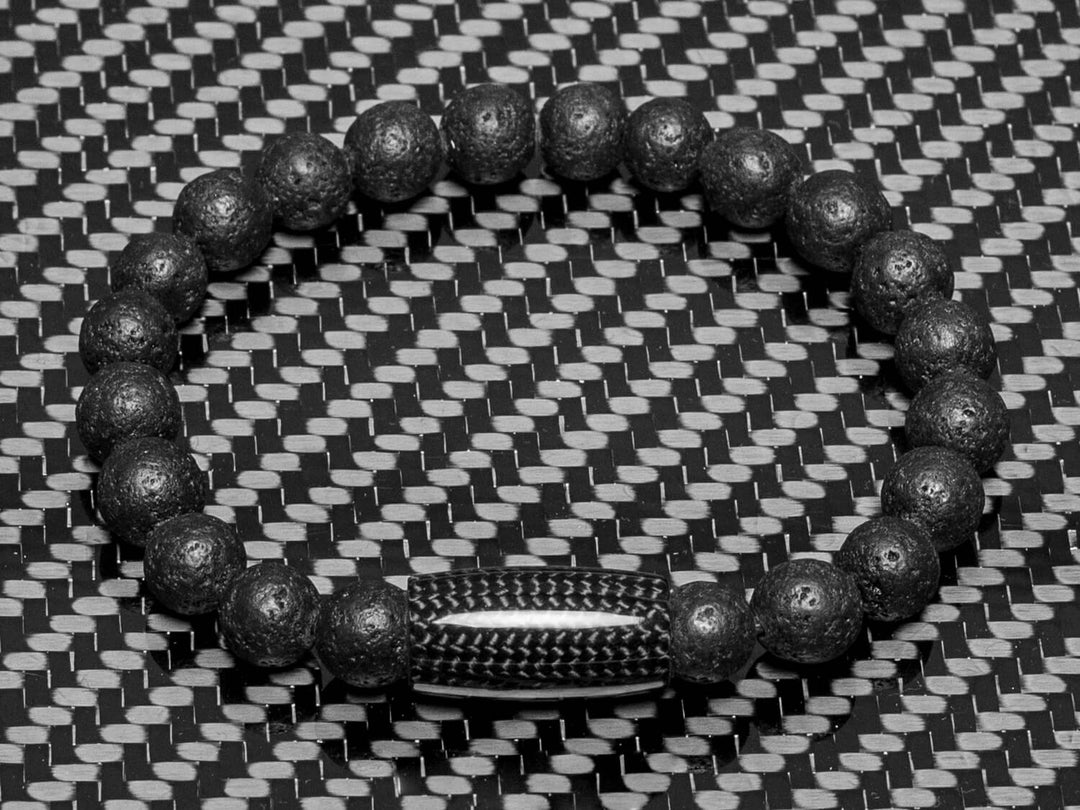 Overhead view of the Carbon Fiber and Lava Rock Beaded Bracelet placed on a carbon fiber background, highlighting the contrast between textured volcanic beads and the polished carbon fiber clasp.