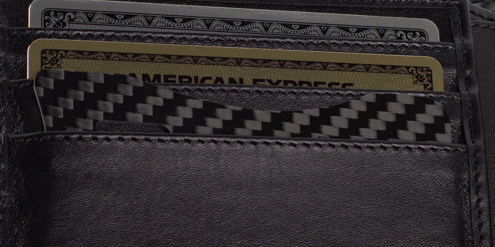 A slim CarbonFG Carbon Fiber Credit Card Bottle Opener snugly inserted in a wallet slot next to credit cards, showcasing its convenient size and stylish carbon fiber weave.