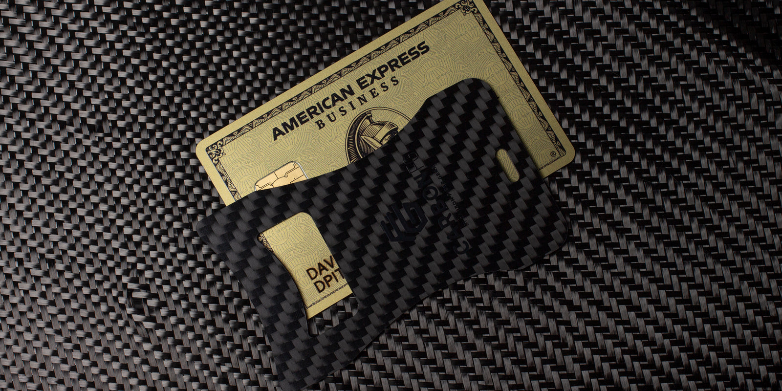 The CarbonFG Carbon Fiber Credit Card Bottle Opener placed on carbon fiber fabric next to a credit card, illustrating its size comparison.